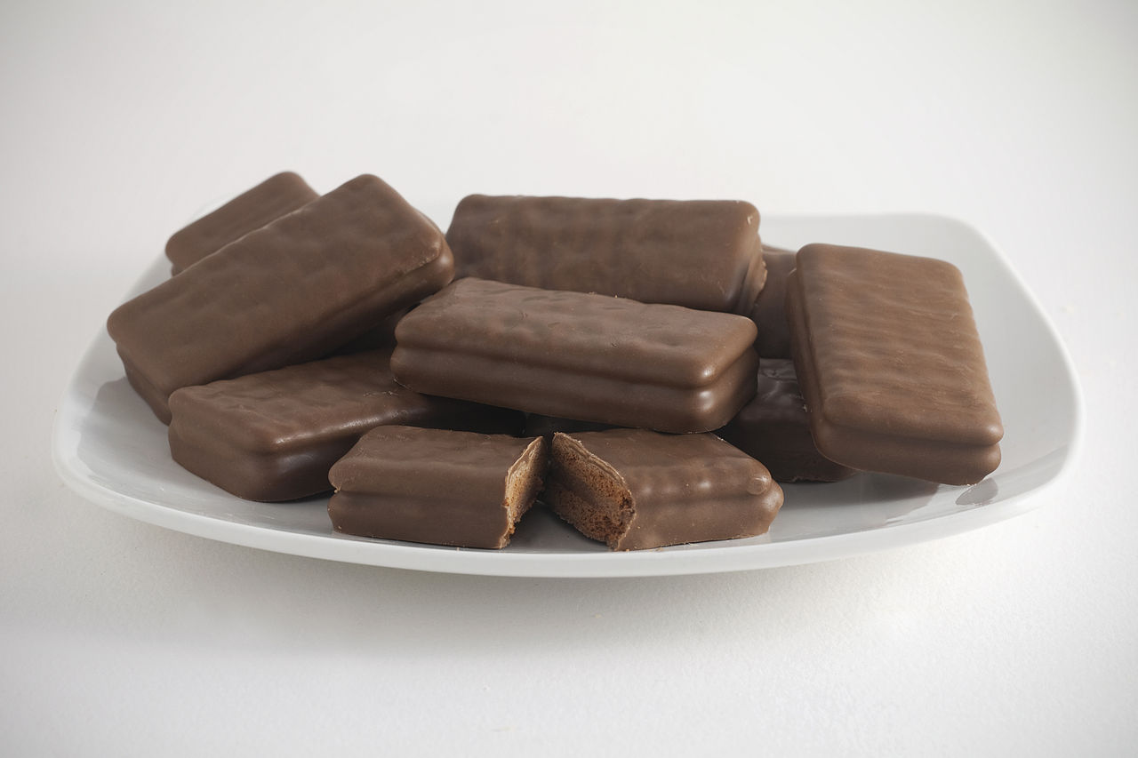 A plate of Tim Tams, with one in the centre broken open to show the biscuit and chocolate cream filling. [Photograph by Bilby](https://commons.wikimedia.org/wiki/File:Tim_Tams.jpg). Licensed under the [Creative Commons Attribution-Share Alike 3.0][creativecommons] license.